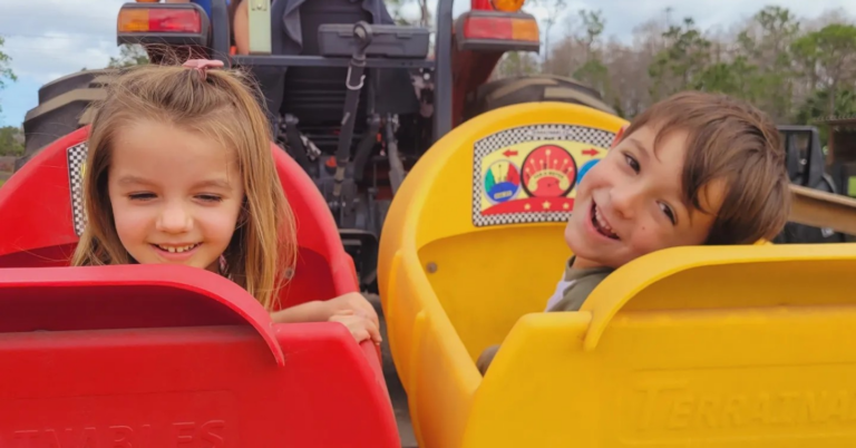 Two smiling children enjoy a colorful tractor ride during a fun-filled birthday party event. This exciting outdoor attraction is perfect for kids' parties and family-friendly events, offering memorable birthday experiences and entertainment for all ages.
