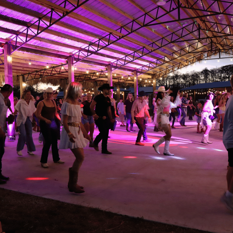 Guests line dancing together during an evening event at the farm pavilion